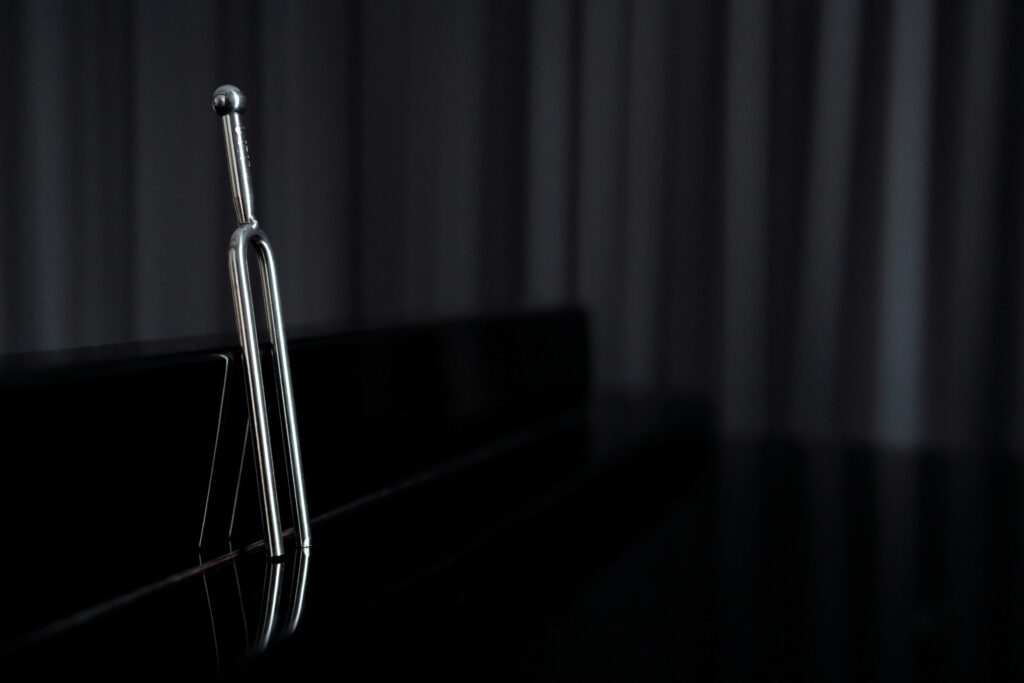 A close-up of a metal tuning fork standing on a reflective piano surface with dark background.